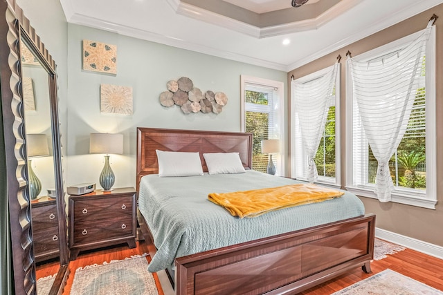 bedroom with hardwood / wood-style flooring, ornamental molding, and a raised ceiling