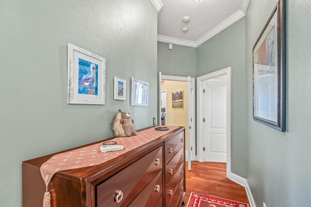 hallway featuring crown molding, a textured ceiling, and light wood-type flooring