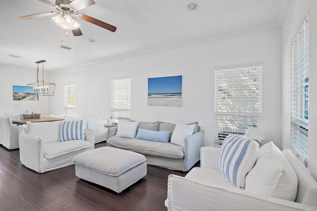 living area with ornamental molding, dark wood-type flooring, ceiling fan with notable chandelier, and visible vents