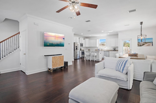 living room featuring dark wood-style floors, visible vents, ornamental molding, and stairway