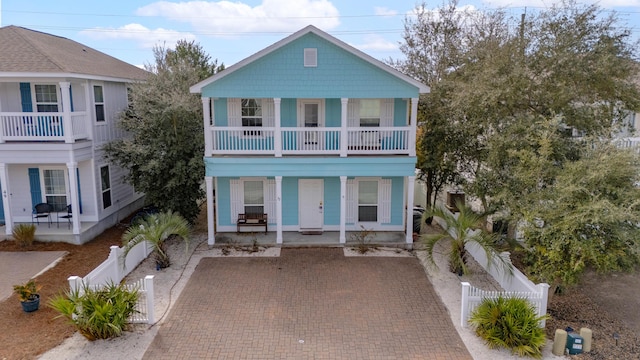 view of front of house featuring a balcony, a fenced front yard, a porch, and decorative driveway