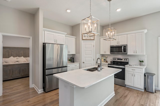 kitchen with sink, white cabinetry, decorative light fixtures, appliances with stainless steel finishes, and an island with sink