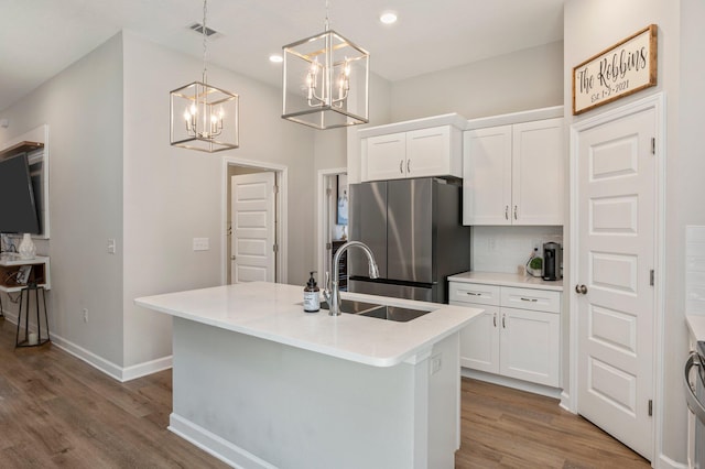 kitchen with pendant lighting, white cabinetry, sink, stainless steel fridge, and a kitchen island with sink