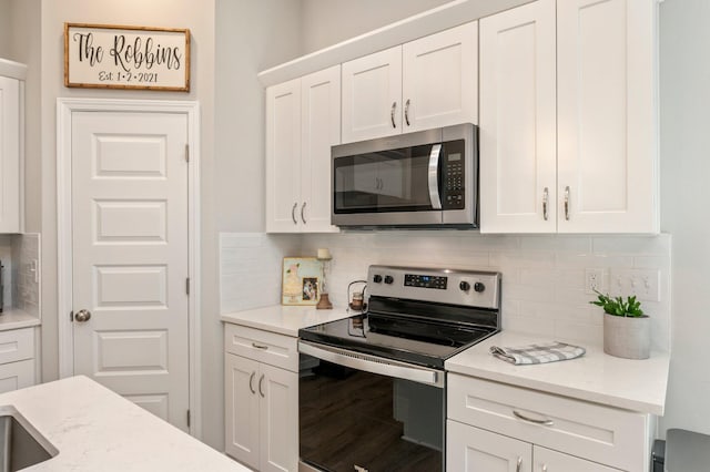 kitchen featuring white cabinetry, wood-type flooring, appliances with stainless steel finishes, light stone countertops, and backsplash