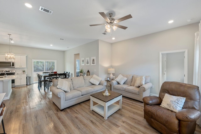 living room with ceiling fan with notable chandelier and light hardwood / wood-style flooring