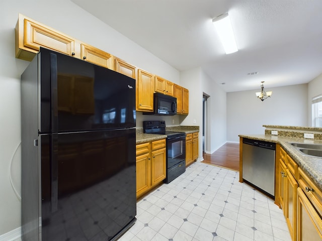 kitchen featuring dark stone counters, black appliances, decorative light fixtures, sink, and an inviting chandelier