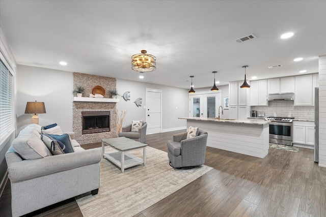 living room with a large fireplace, baseboards, visible vents, dark wood-style flooring, and recessed lighting