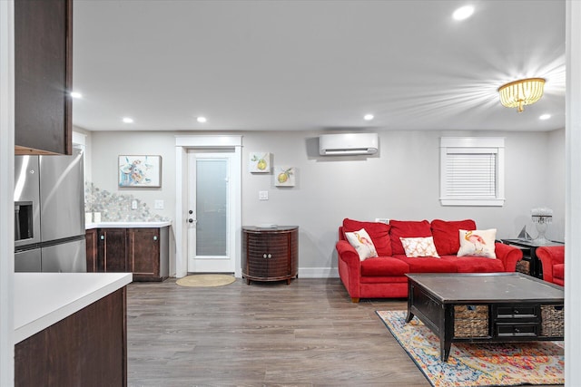 living room with a wall unit AC, baseboards, wood finished floors, and recessed lighting