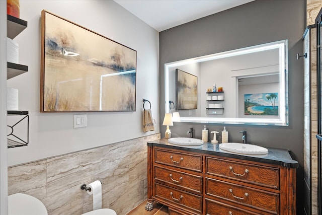 full bath featuring double vanity, a sink, toilet, and tile walls