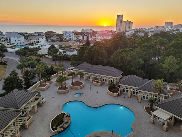 pool at dusk featuring a patio area, a water view, a community pool, and a city view