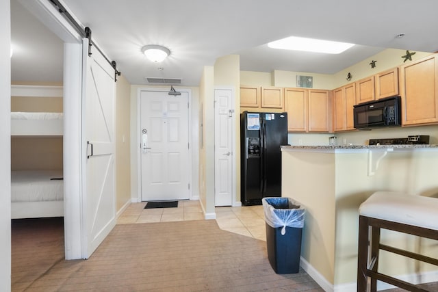 kitchen featuring a breakfast bar area, black appliances, light tile patterned flooring, light brown cabinetry, and a barn door