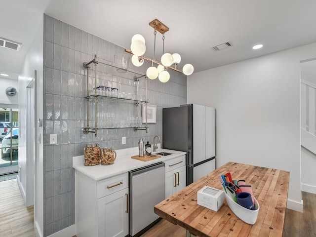 kitchen featuring stainless steel refrigerator, white cabinetry, sink, tile walls, and dishwashing machine