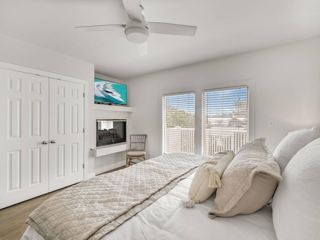 bedroom featuring wood-type flooring, a multi sided fireplace, ceiling fan, and a closet