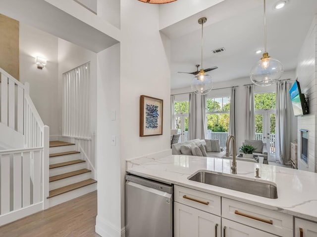 kitchen with sink, decorative light fixtures, dishwasher, light stone countertops, and white cabinets