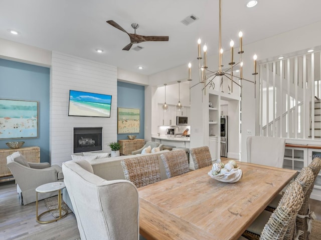 dining area with ceiling fan, a large fireplace, and light hardwood / wood-style flooring