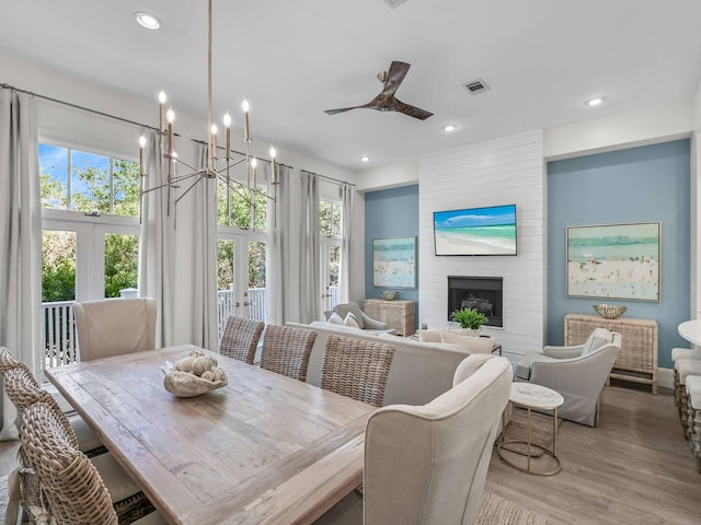 dining area featuring ceiling fan with notable chandelier, a fireplace, light hardwood / wood-style floors, and french doors