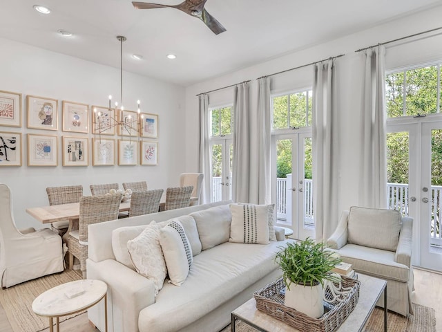 living room featuring ceiling fan with notable chandelier, plenty of natural light, french doors, and light wood-type flooring