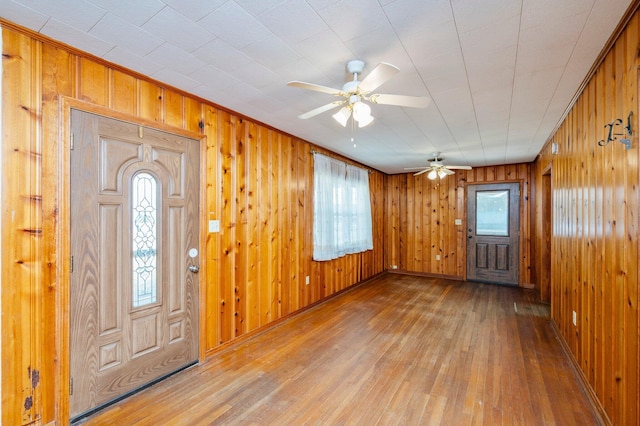 foyer entrance with hardwood / wood-style flooring, ceiling fan, and wooden walls