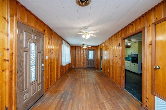 entrance foyer featuring wood-type flooring, ceiling fan, and wooden walls
