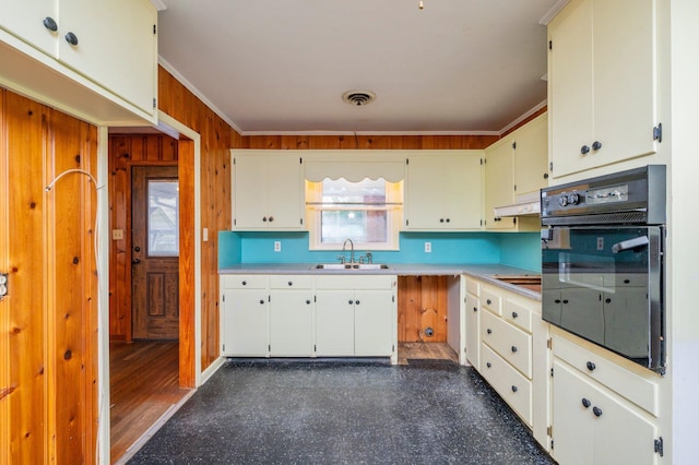 kitchen featuring wall oven, sink, crown molding, and wooden walls
