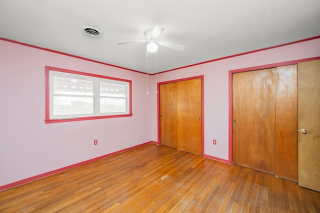 unfurnished bedroom with multiple closets, wood-type flooring, and ornamental molding