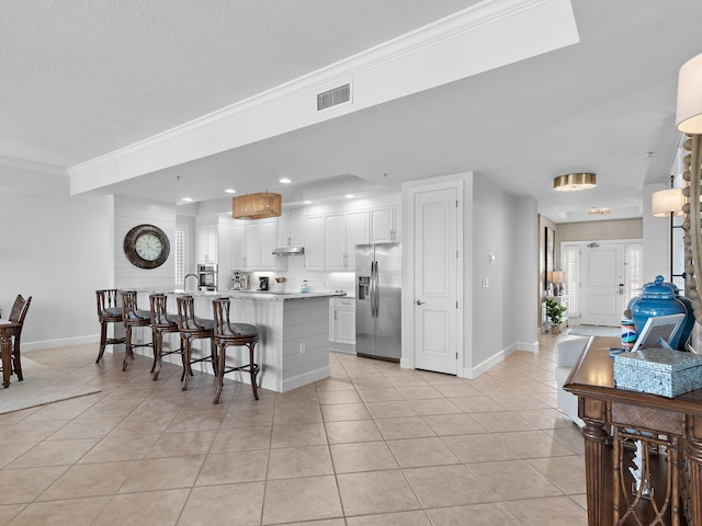 kitchen with a breakfast bar area, white cabinetry, stainless steel refrigerator with ice dispenser, a kitchen island, and light tile patterned flooring