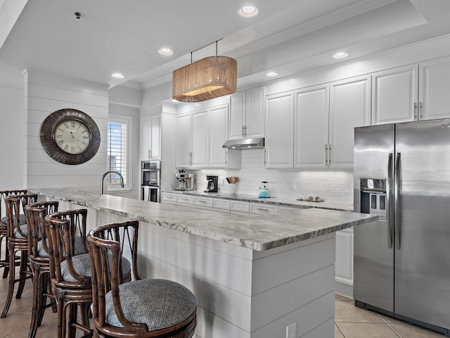 kitchen featuring a kitchen bar, white cabinetry, hanging light fixtures, appliances with stainless steel finishes, and backsplash