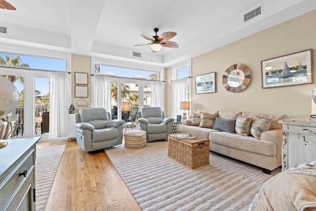 living room with a raised ceiling, plenty of natural light, ceiling fan, and light hardwood / wood-style flooring