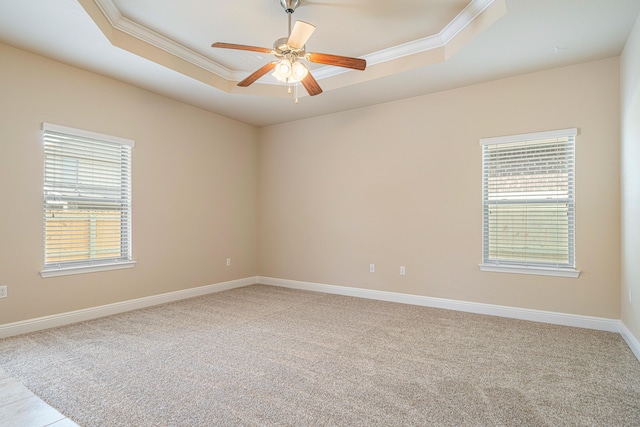 empty room featuring crown molding, ceiling fan, baseboards, a tray ceiling, and light carpet