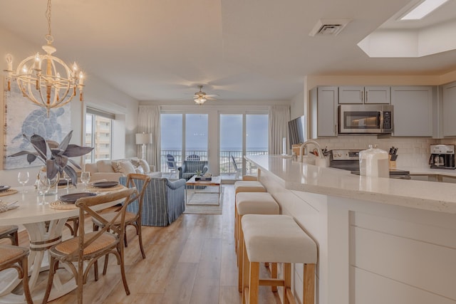 kitchen featuring gray cabinetry, light hardwood / wood-style flooring, stainless steel appliances, light stone countertops, and decorative backsplash