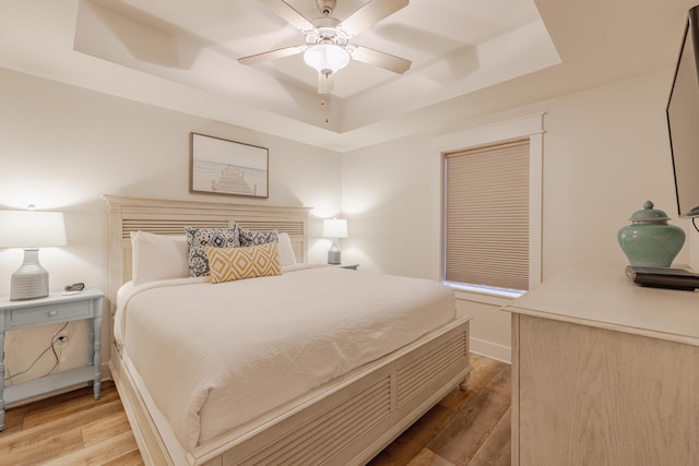 bedroom with a raised ceiling, ceiling fan, and light hardwood / wood-style floors