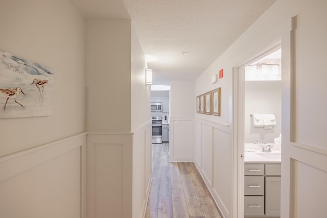 hall with sink, light hardwood / wood-style floors, and a textured ceiling