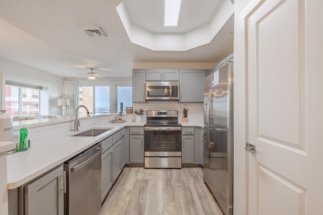 kitchen featuring sink, gray cabinetry, light hardwood / wood-style flooring, a raised ceiling, and stainless steel appliances