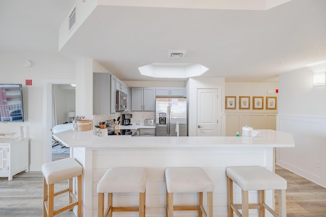 kitchen with appliances with stainless steel finishes, gray cabinetry, backsplash, a kitchen bar, and light hardwood / wood-style floors