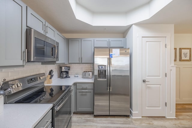 kitchen with light stone counters, gray cabinets, stainless steel appliances, light hardwood / wood-style floors, and decorative backsplash