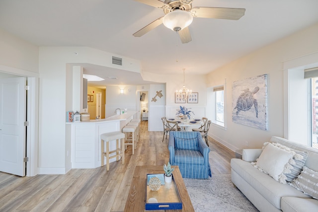 living room with ceiling fan with notable chandelier and light hardwood / wood-style floors