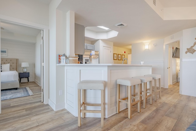 kitchen with stainless steel fridge with ice dispenser, sink, a breakfast bar area, light hardwood / wood-style floors, and kitchen peninsula