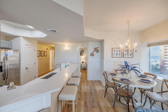 dining room featuring sink, a chandelier, a textured ceiling, and light hardwood / wood-style floors