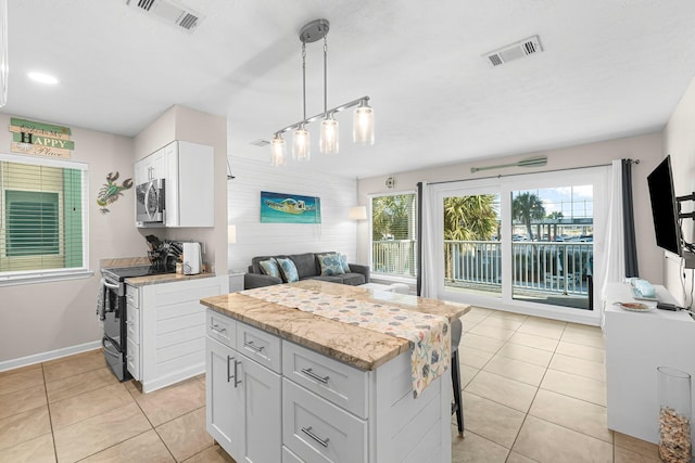 kitchen featuring light tile patterned floors, stainless steel appliances, white cabinets, a kitchen island, and decorative light fixtures