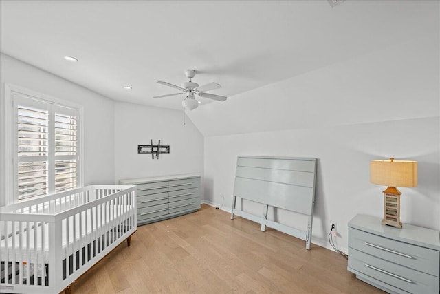 bedroom with lofted ceiling, a crib, light hardwood / wood-style flooring, and ceiling fan