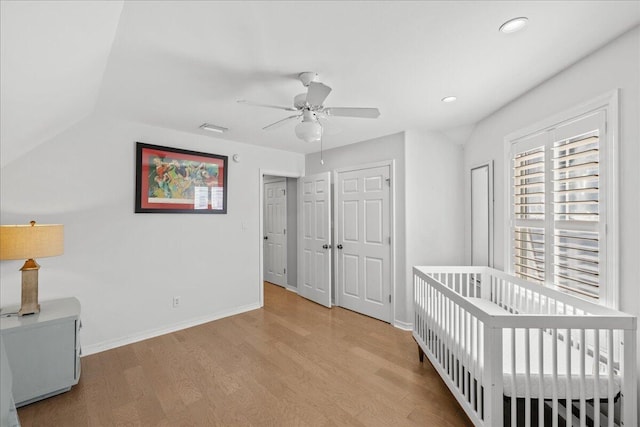 unfurnished bedroom featuring ceiling fan, lofted ceiling, light hardwood / wood-style flooring, and a crib