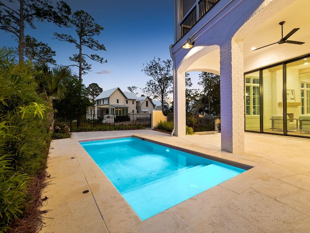 pool at dusk featuring ceiling fan and a patio area