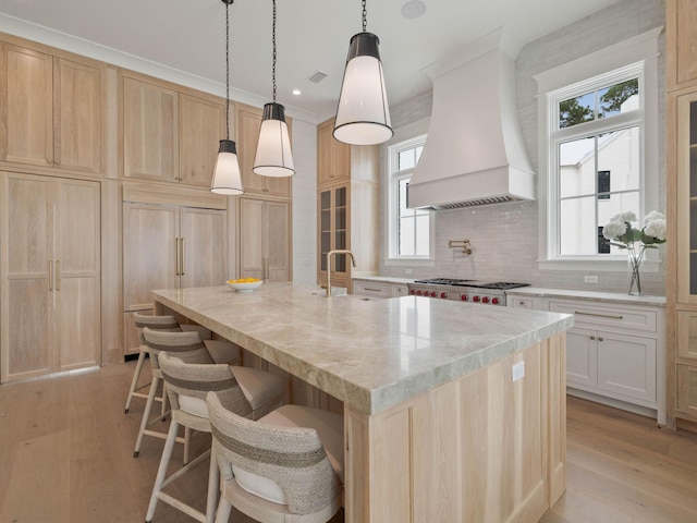 kitchen featuring premium range hood, a breakfast bar, a center island with sink, and light wood-type flooring