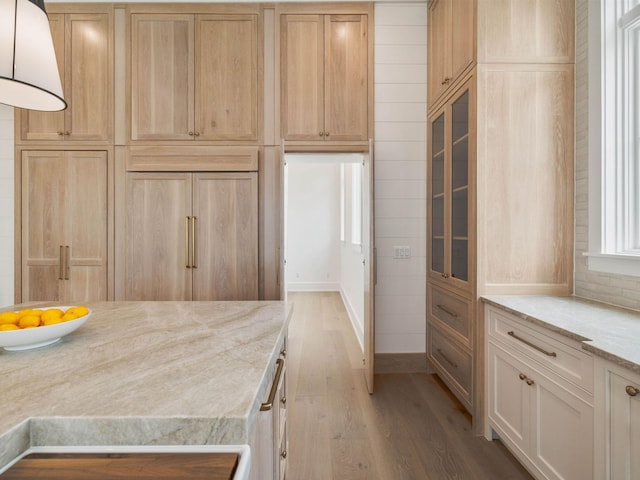 kitchen with paneled refrigerator, light hardwood / wood-style floors, light stone counters, and light brown cabinets