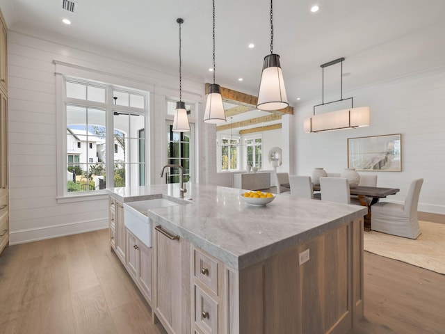 kitchen with pendant lighting, sink, light stone countertops, a large island with sink, and light wood-type flooring