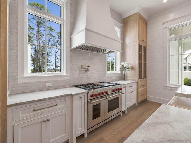 kitchen featuring light stone counters, range with two ovens, custom exhaust hood, and white cabinets