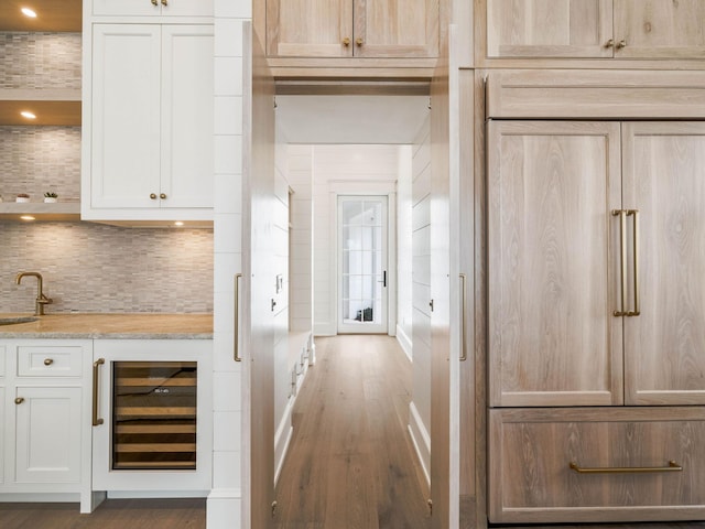 interior space with sink, white cabinetry, hardwood / wood-style flooring, beverage cooler, and decorative backsplash