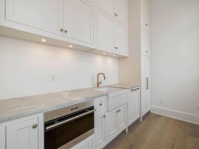 kitchen featuring white cabinetry, sink, oven, light stone counters, and light hardwood / wood-style floors