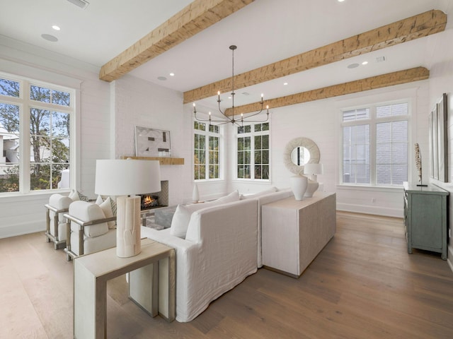 living room featuring beamed ceiling, an inviting chandelier, hardwood / wood-style floors, and a fireplace