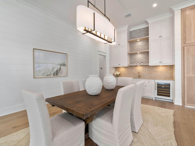 dining area with wine cooler, ornamental molding, and light hardwood / wood-style floors